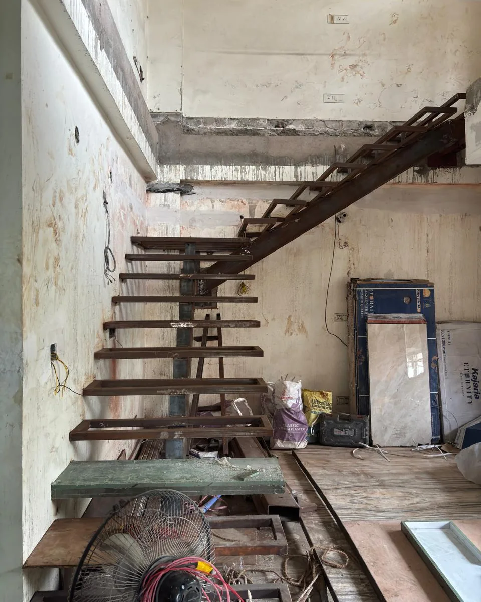 Later in fit-out: a steel stair now rises through the opening, with materials and tools still on the floor.